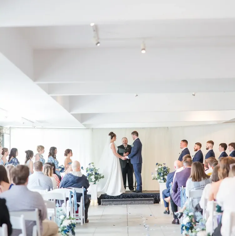 A bride and groom on the altar in a bright white room with guests in rows of chairs at Castle Farms.