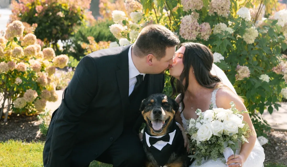 Bride and groom kissing with their dog in the Castle Farms garden. Photo credit: Jazmin G Photo.