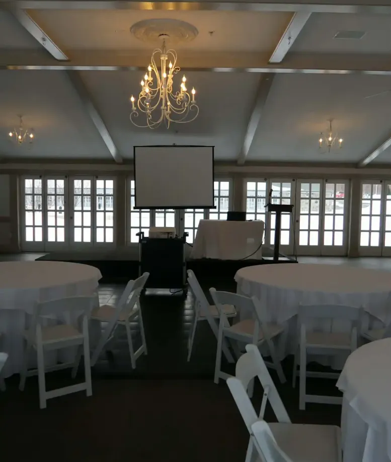 Tables and chairs in front of a rollout presentation screen in an event space at Castle Farms.