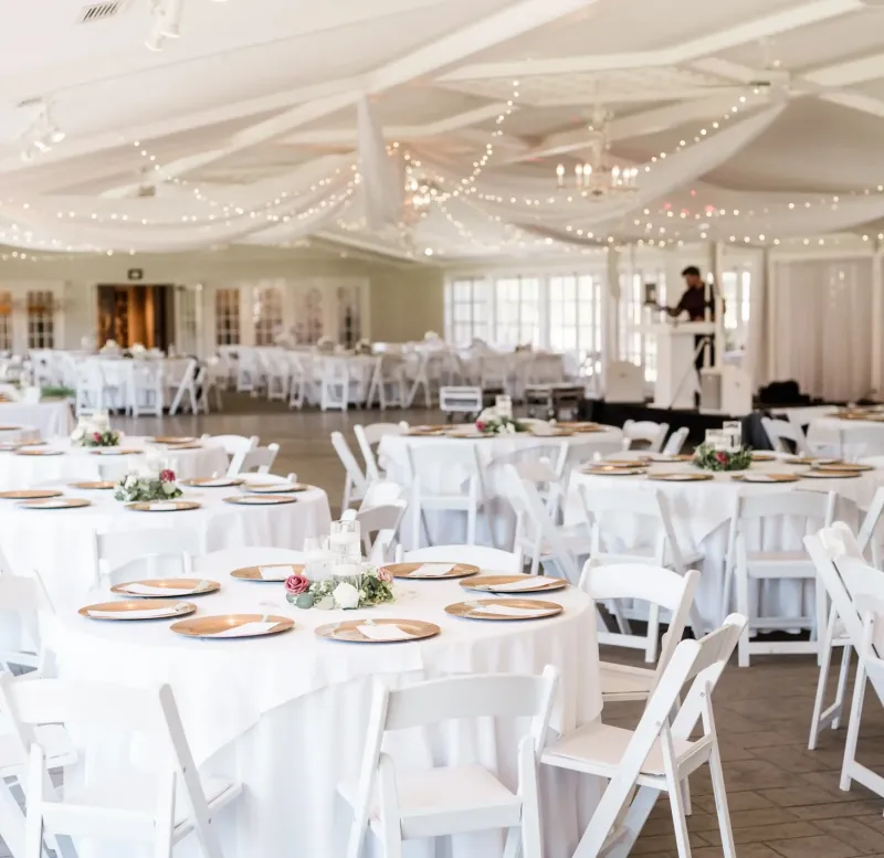 The East Garden Room with white tables and chairs and stage equipment at Castle Farms.