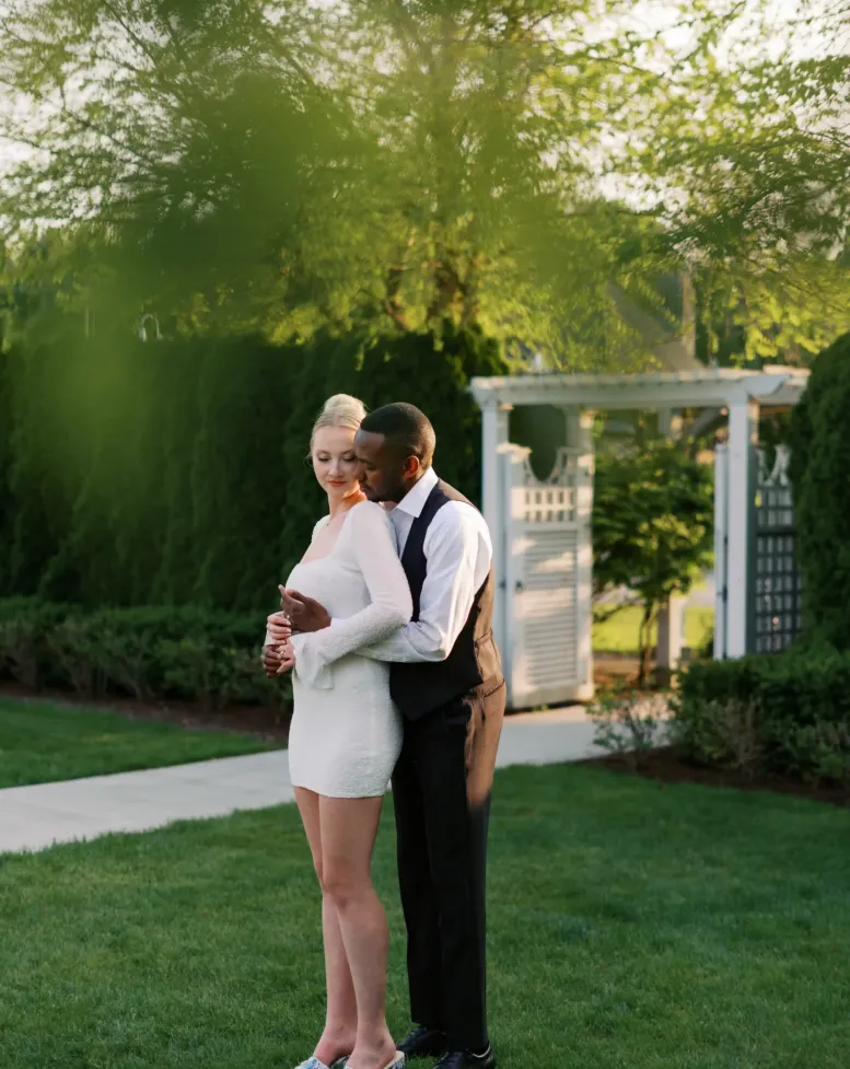 A couple posing together in a green garden with hedges and trees at Castle Farms.