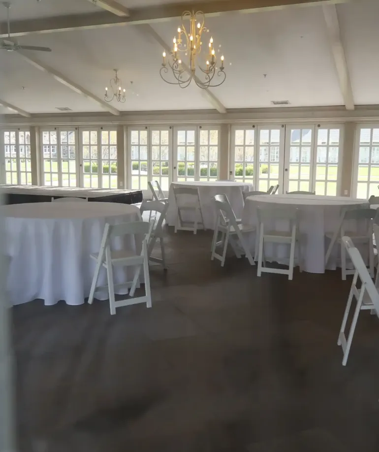 Tables and chairs in a sunroom with chandeliers and windows at Castle Farms.