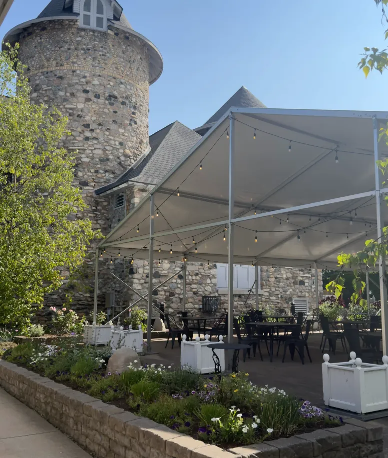 A side view of people chatting in the Rose tent next to a stone tower at Castle Farms.