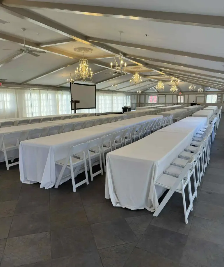 Long white tables and white chairs set up in front of a screen in an event space at Castle Farms. 