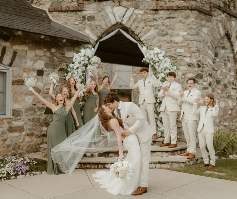 A groom dipping his bride with the wedding party celebrating in the background in a courtyard at Castle Farms.