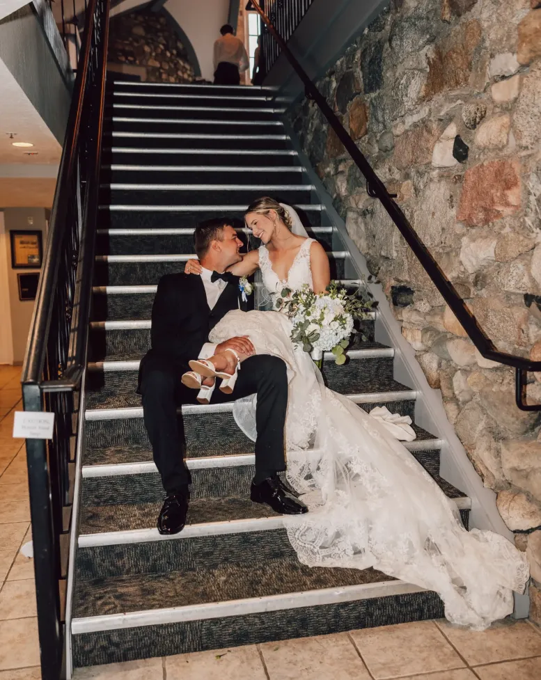 A bride and groom sitting and embracing on a staircase inside an event space in Castle Farms.