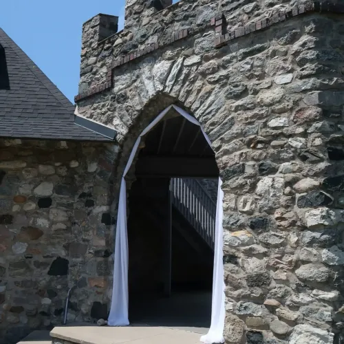 A stone tower with an archway decorated with draping white fabric at Castle Farms.