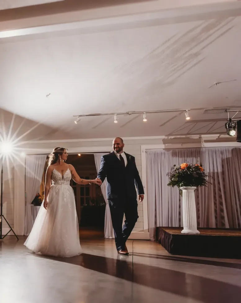 A couple enters the dance floor holding hands under a spotlight in a reception hall at Castle Farms.