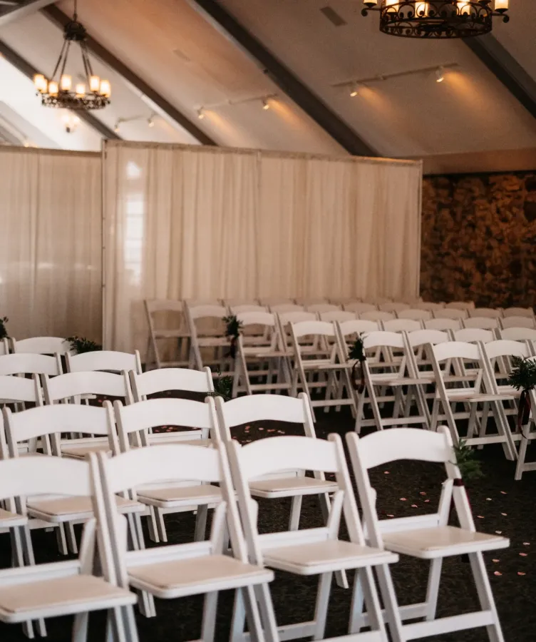 White chairs in rows inside a golden-lit wedding venue at Castle Farms.