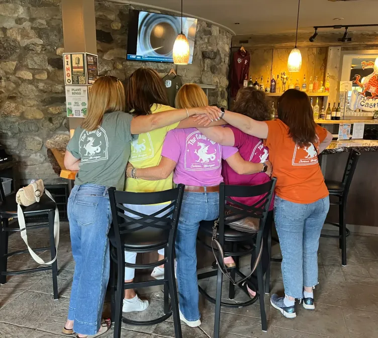 Employees with different color Castle Farms t-shirts standing side by side facing the bar at the pub at Castle Farms.