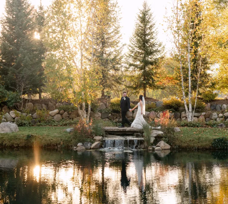 A bride and groom walking by a pond and trees at sunset at Castle Farms.
