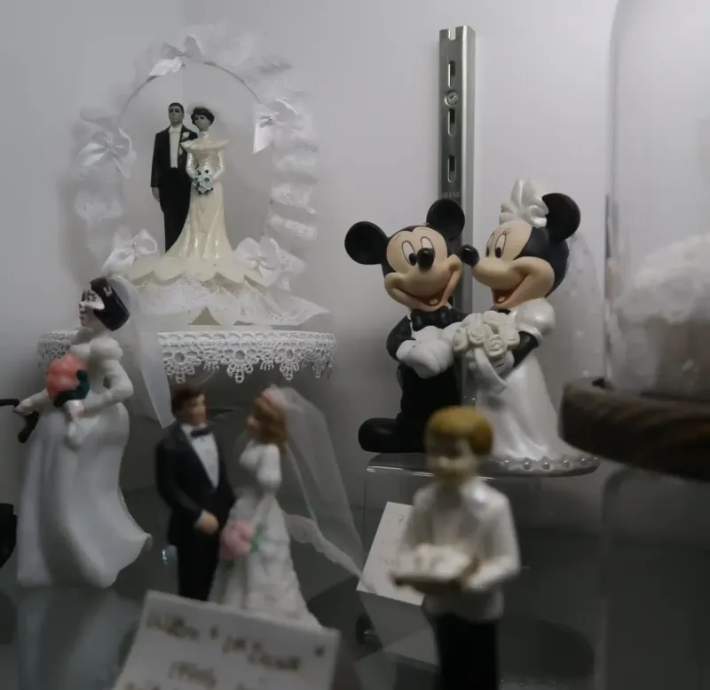 A collection of wedding toppers, including Mickey and Minnie Mouse toppers, in a cabinet at Castle Farms.