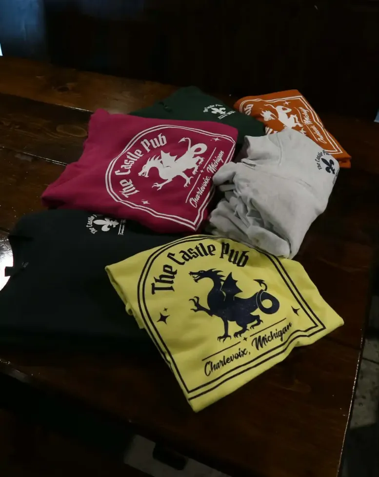 Folded Castle Pub shirts on a wooden table at Castle Farms. 
