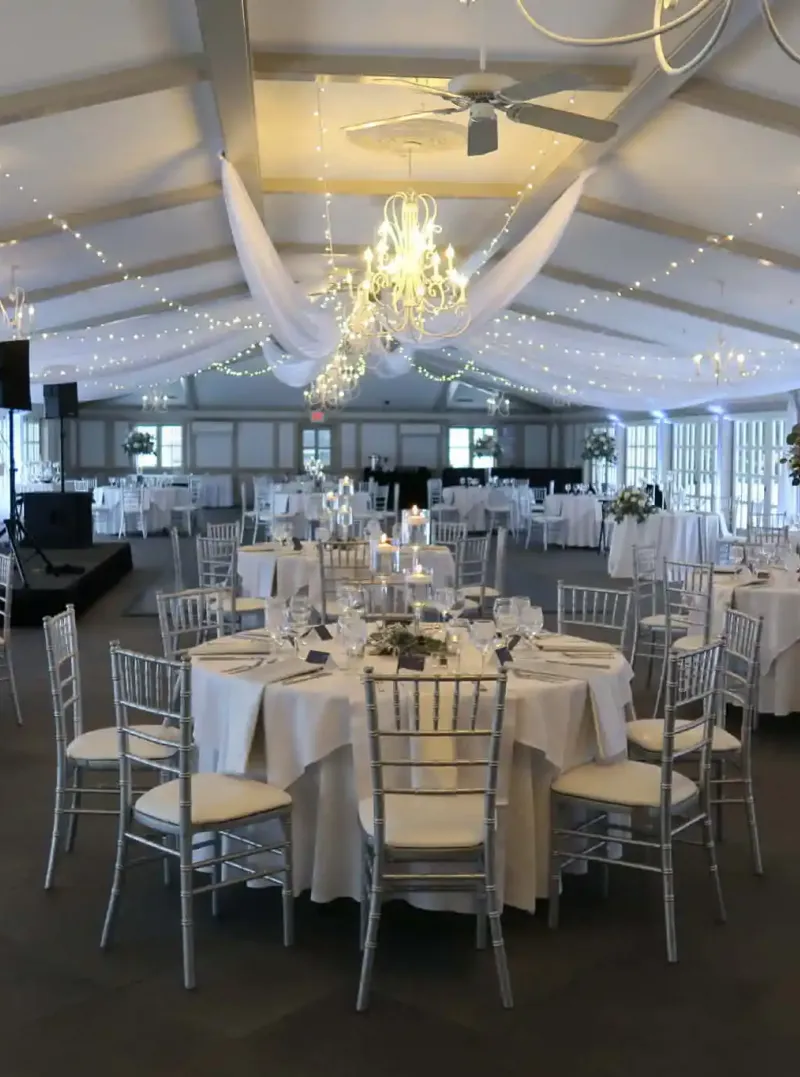 A white event space with tables and chairs under a chandelier at Castle Farms.
