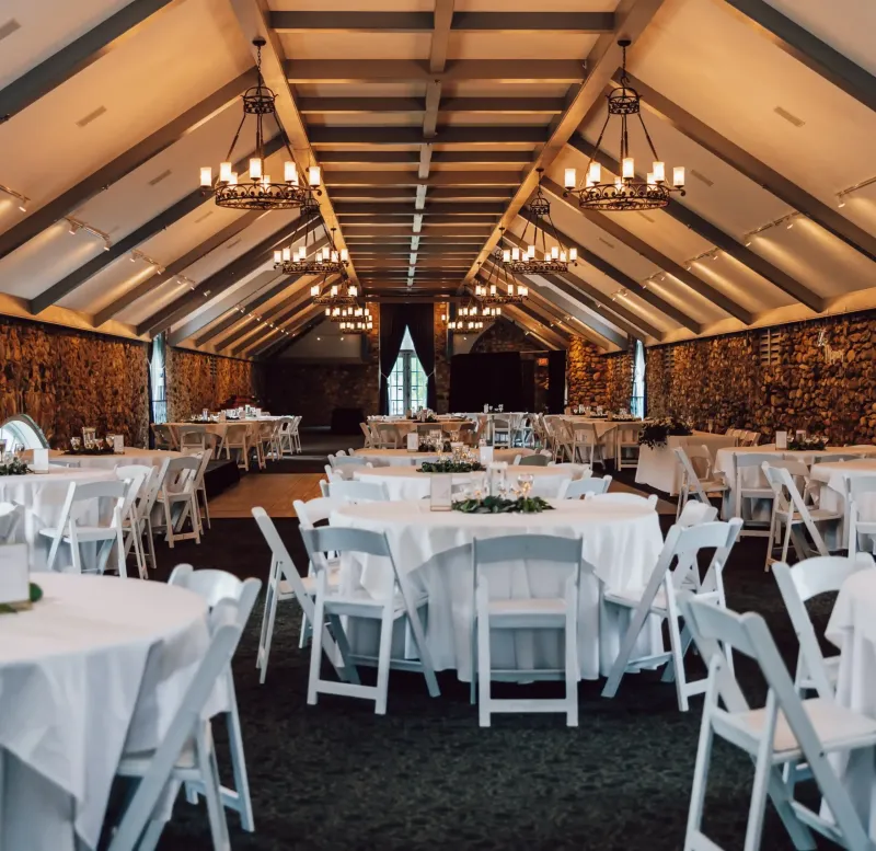 An event space with tables and chairs with golden light shining from chandeliers at Castle Farms.