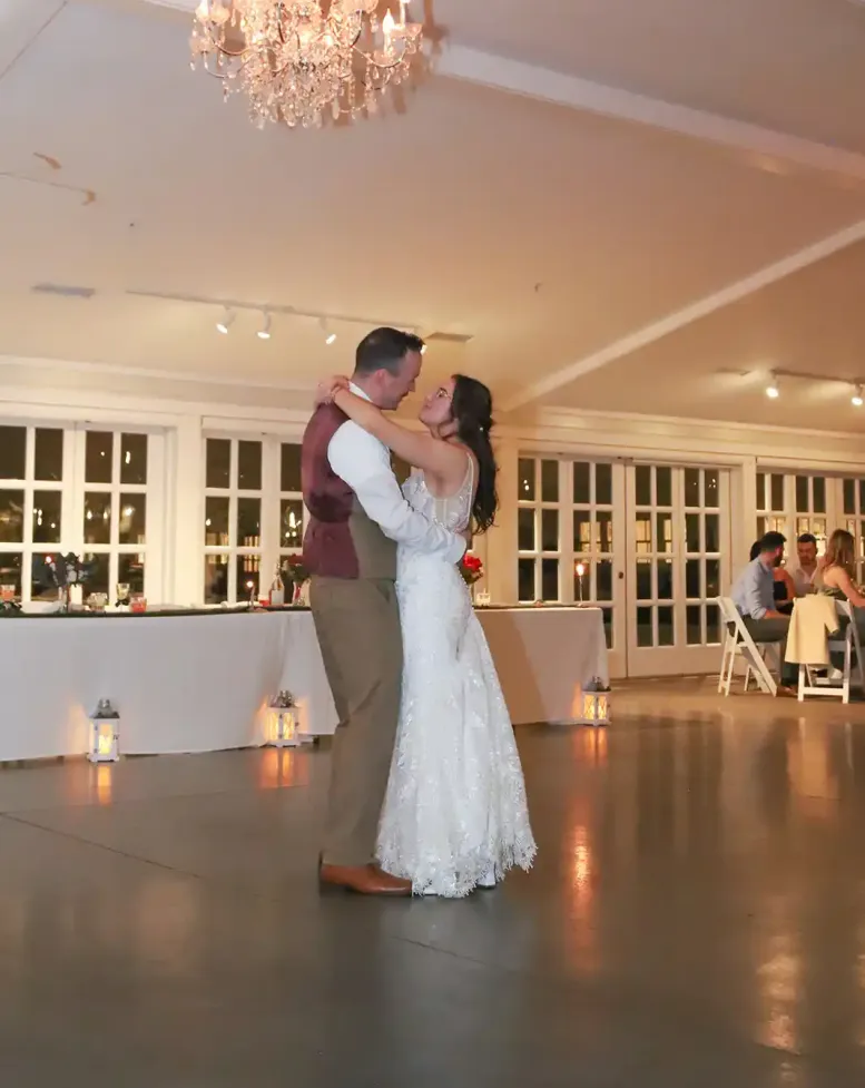 A bride and groom dancing on the dance floor under an ornate chandelier in a bright event space at Castle Farms.