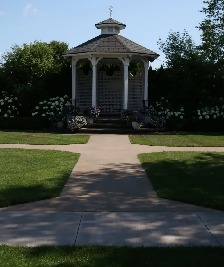 A sidewalk leading to a tall white gazebo surrounded by trees. 