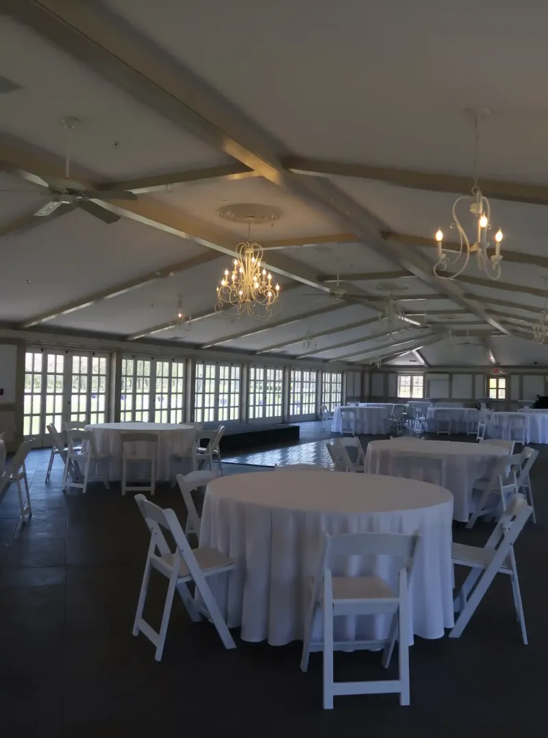 Chairs and tables in a dimly lit room with golden chandeliers in an event space at Castle Farms.