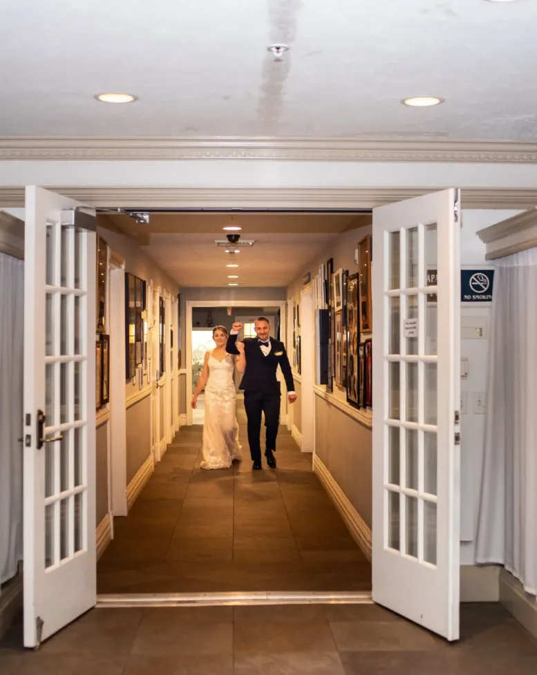 A bride and groom walking down a hallway to open doors of a reception hall at Castle Farms. 
