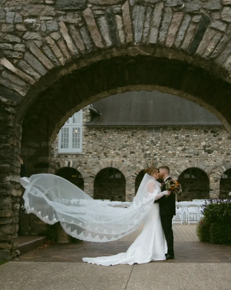A bride and groom kissing under a stone archway at Castle Farms.