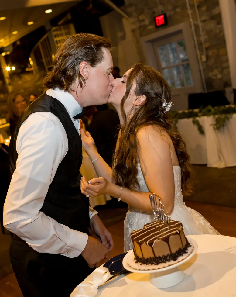 A bride and groom embracing next to a chocolate cake at a reception in an event space at Castle Farms.