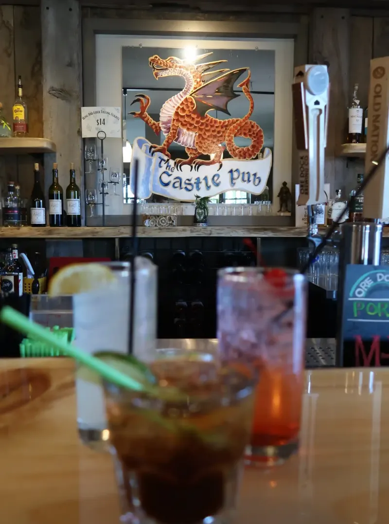 Drinks in glasses on a wooden bar in front of a red dragon painting at the pub at Castle Farms. 