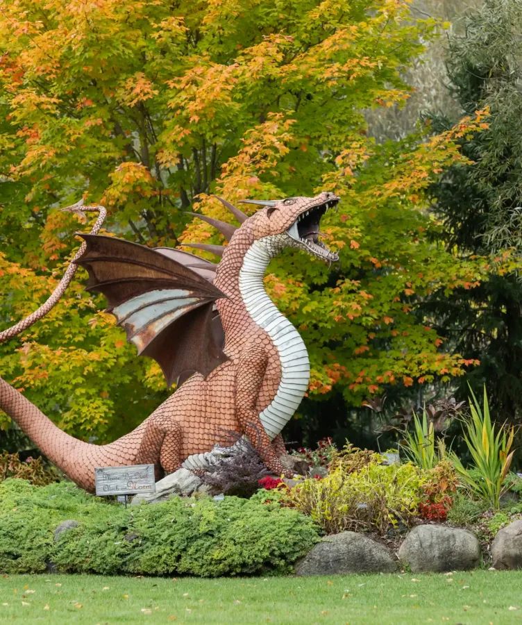 A dark orange dragon statue in front of a grove of trees at Castle Farms.