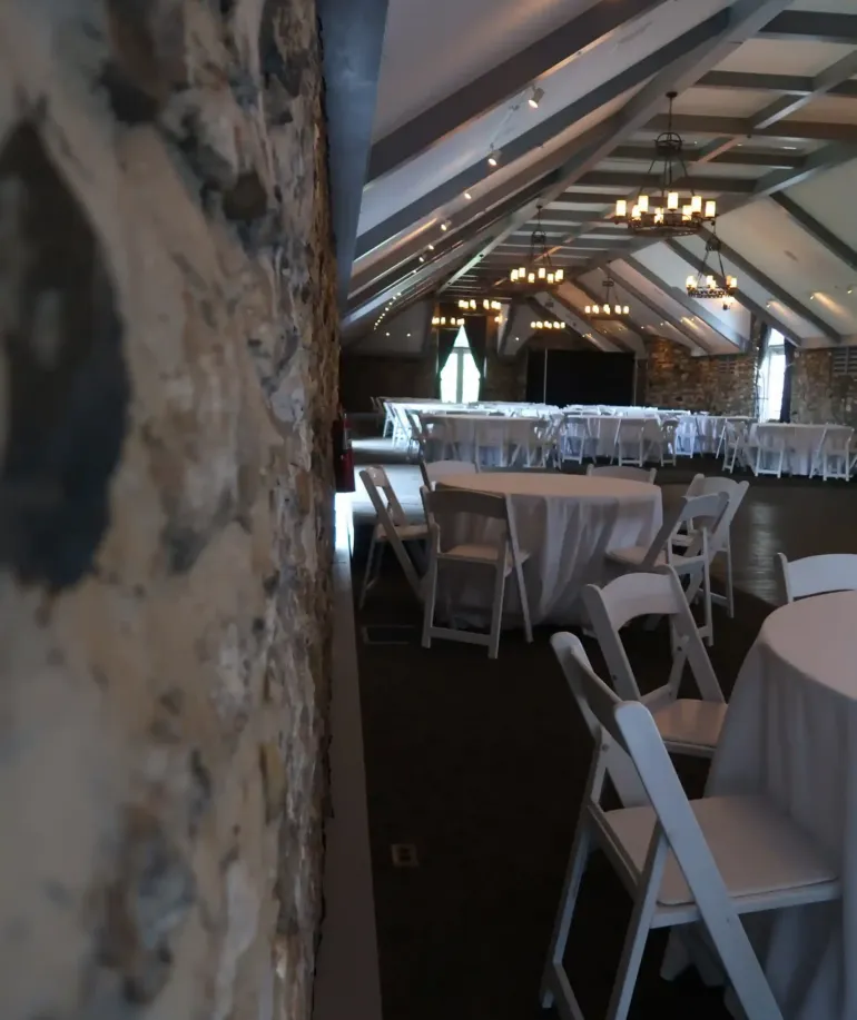 The side of a stone wall and some chairs and tables in an event space at Castle Farms.