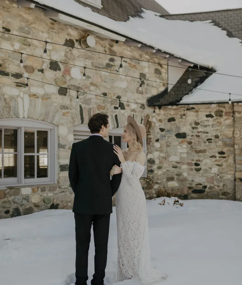 Wedding couple standing together in the snow beside a stone building at Castle Farms. Photo credit: Alexis Brianne Photography.