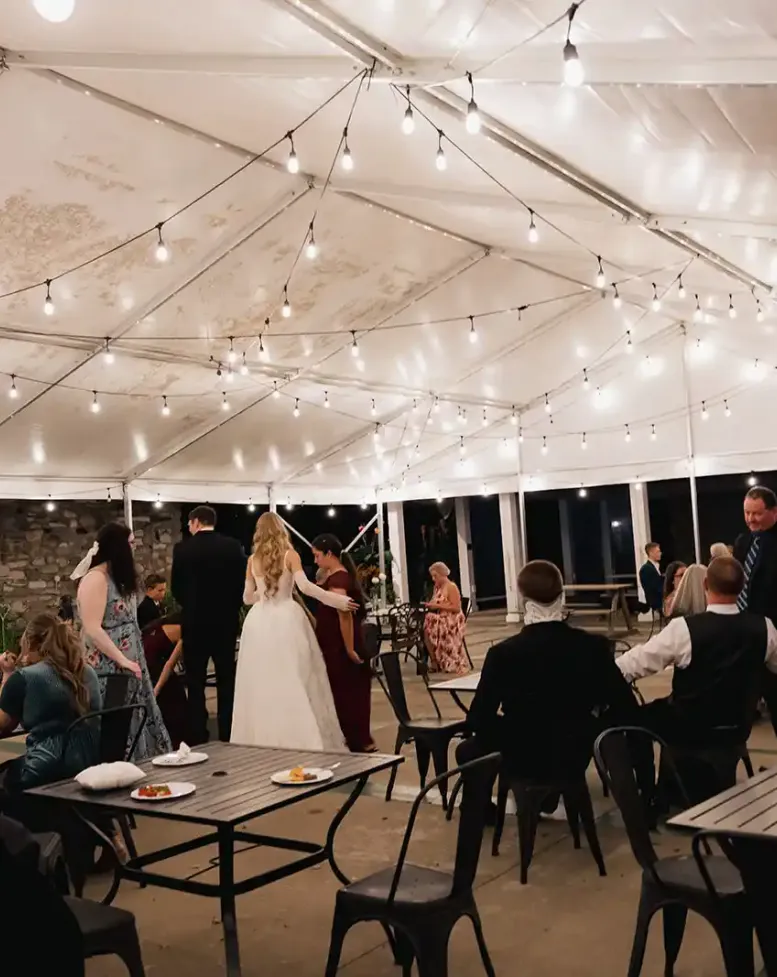 Guests and a bride at a  wedding reception under a white tent outside at night at Castle Farms.