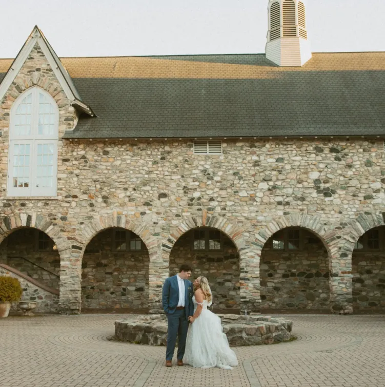 A bride and groom standing in front of a fountain in an empty stone courtyard at Castle Farms.