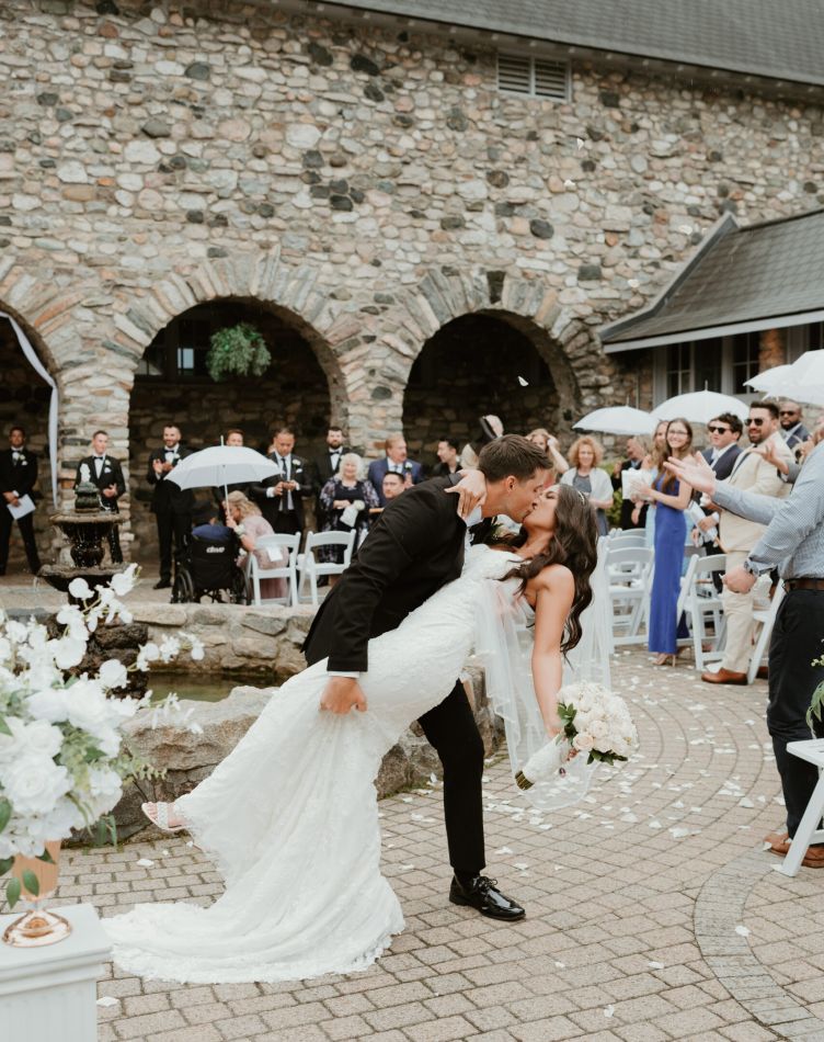 A groom dips his bride in front of the audience after a wedding in a courtyard at Castle Farms.