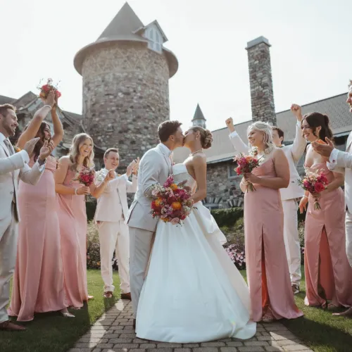 Bride and groom kissing as their wedding party celebrates in front of the Castle Farms stone towers. Photo credit: Elisabeth Joy Photography.