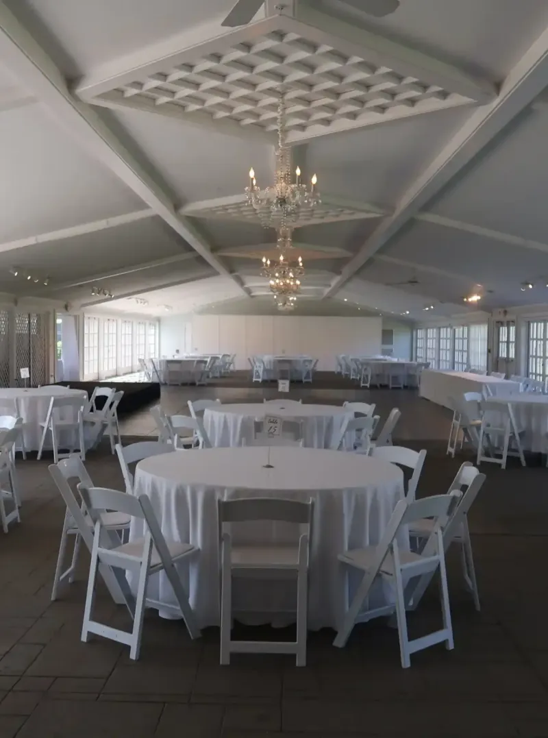 A white event space with windows and white tables and chairs at Castle Farms.