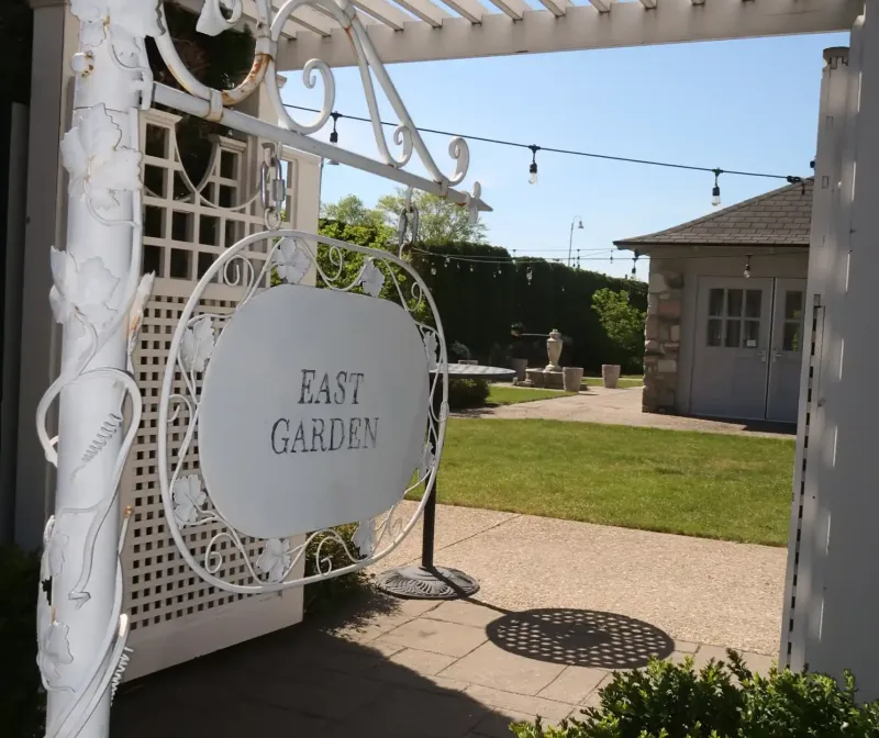 A white sign labeled "East Garden" pointing to a yard and sidewalk leading to the East Garden Room at Castle Farms.