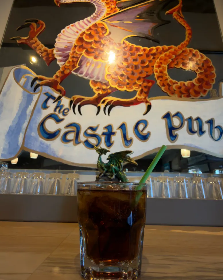 A drink on a wooden bar in front of a red dragon painting at the pub at Castle Farms.