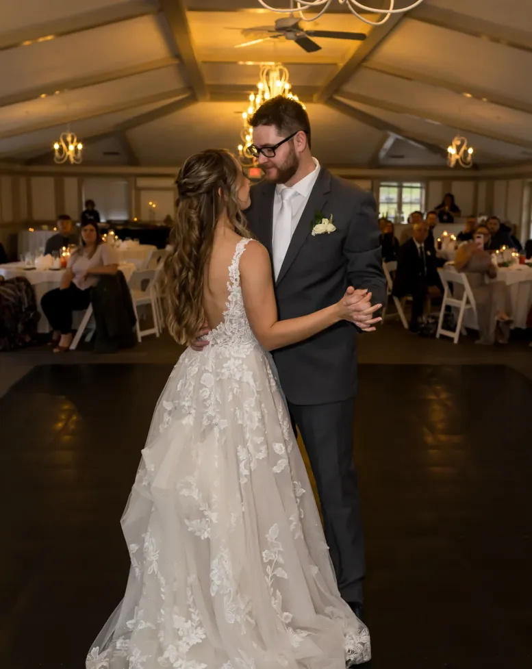 A bride and groom dancing slowly under a chandelier in a warm-lighted reception hall at Castle Farms.