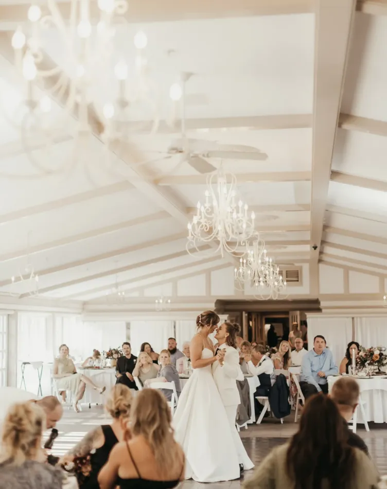 A couple dances on the dance floor with wedding guests watching in a bright reception space with crystal chandeliers at Castle Farms.