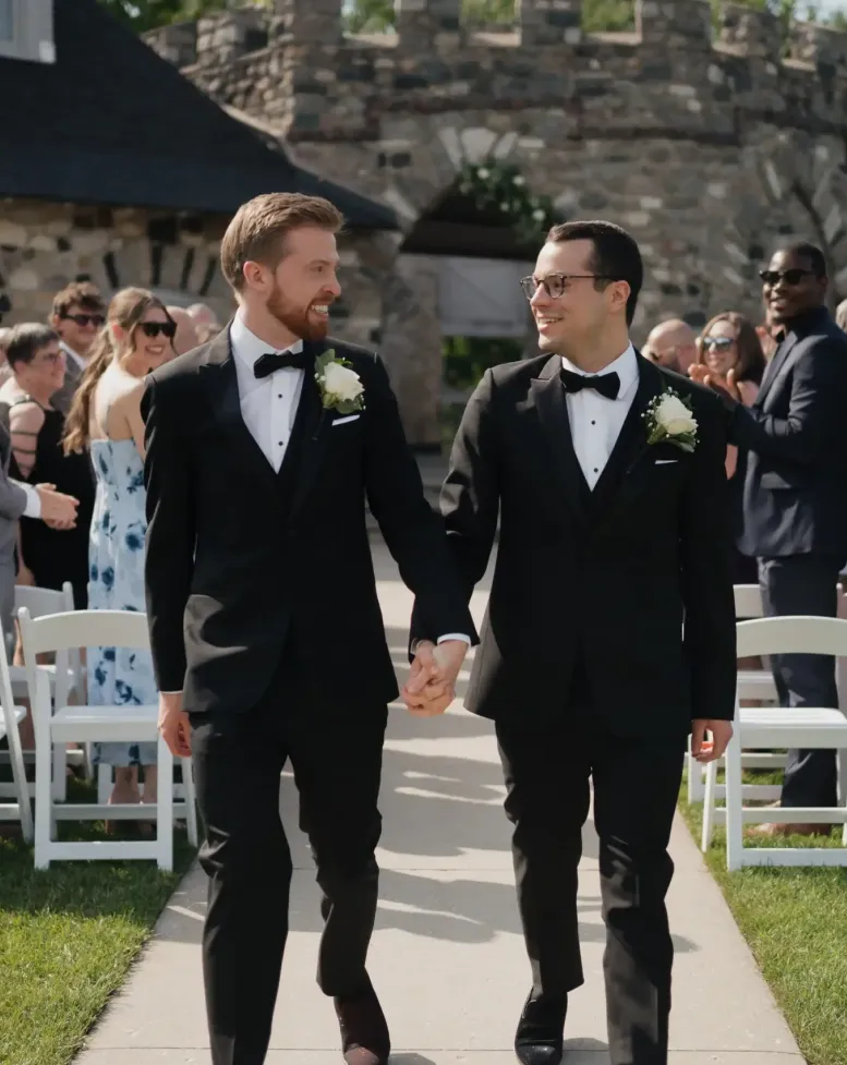 Grooms walking hand-in-hand after a wedding in a courtyard at Castle Farms. 