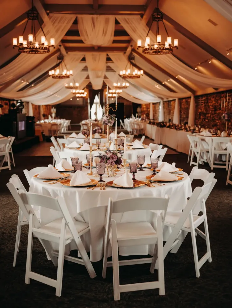 A table set with decorations under golden light from chandeliers in an event space at Castle Farms.