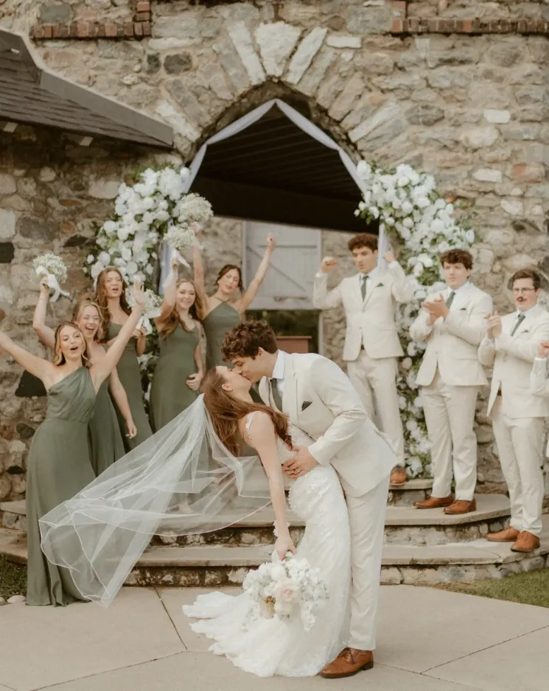 A groom dipping his bride with the wedding party celebrating in the background in a courtyard at Castle Farms.