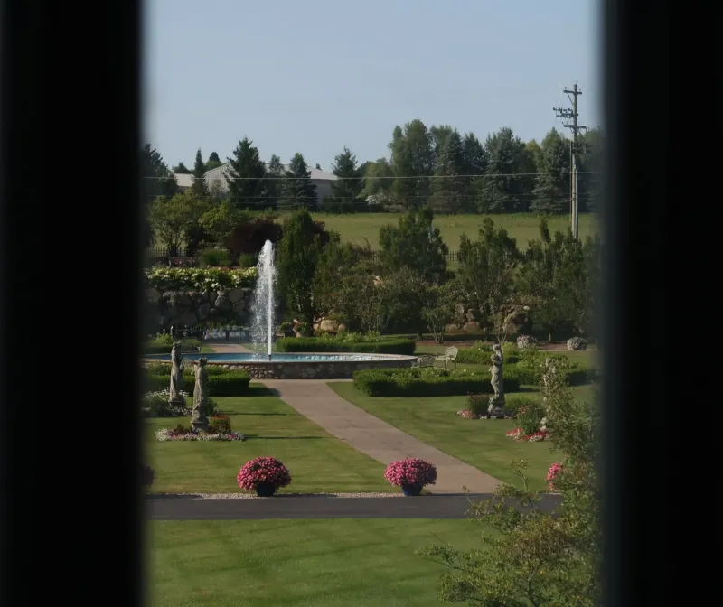 A view of a water fountain and the grounds from a window at Castle Farms.