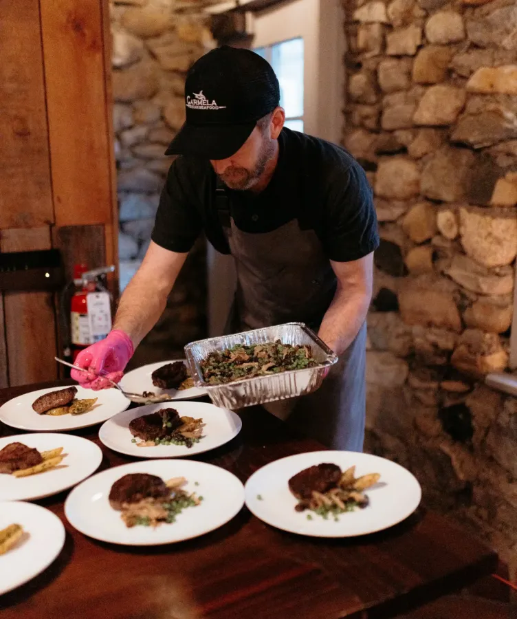A man distributes food onto plates on a wooden table at Castle Farms.