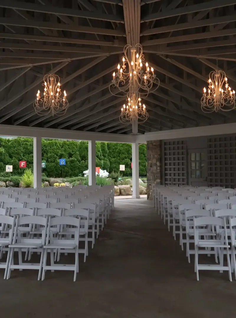 Rows of white chairs under chandeliers in the Rose Pavilion at Castle Farms.