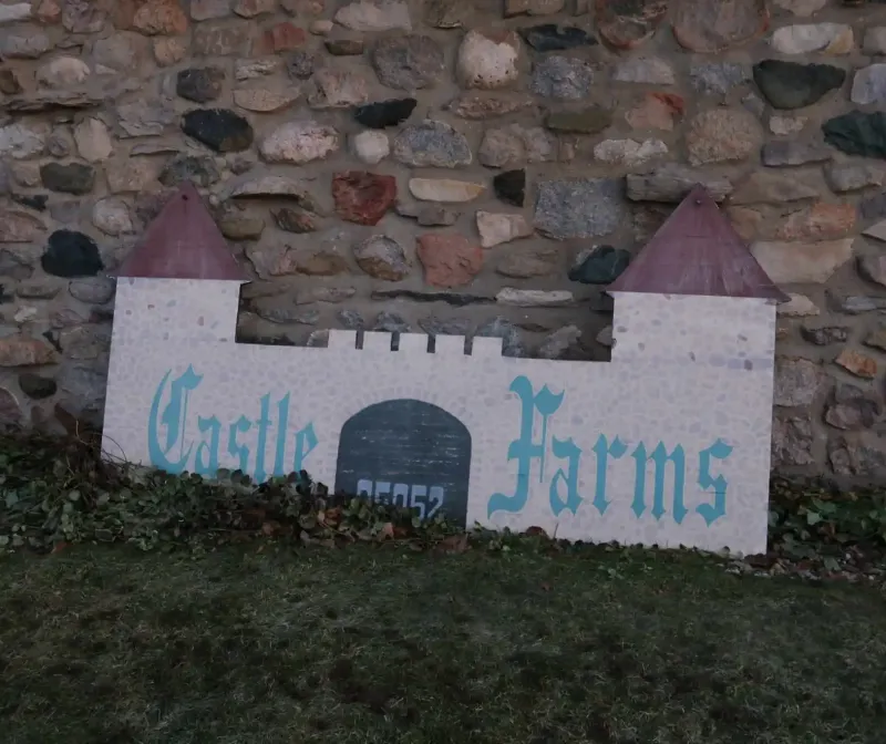 A castle-shaped, painted sign labeled "Castle Farms" leaning on a stone wall at Castle Farms. 
