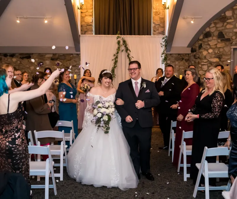 A bride and groom walking down the aisle with guests throwing rose petals in their path in a chapel wedding venue at Castle Farms.