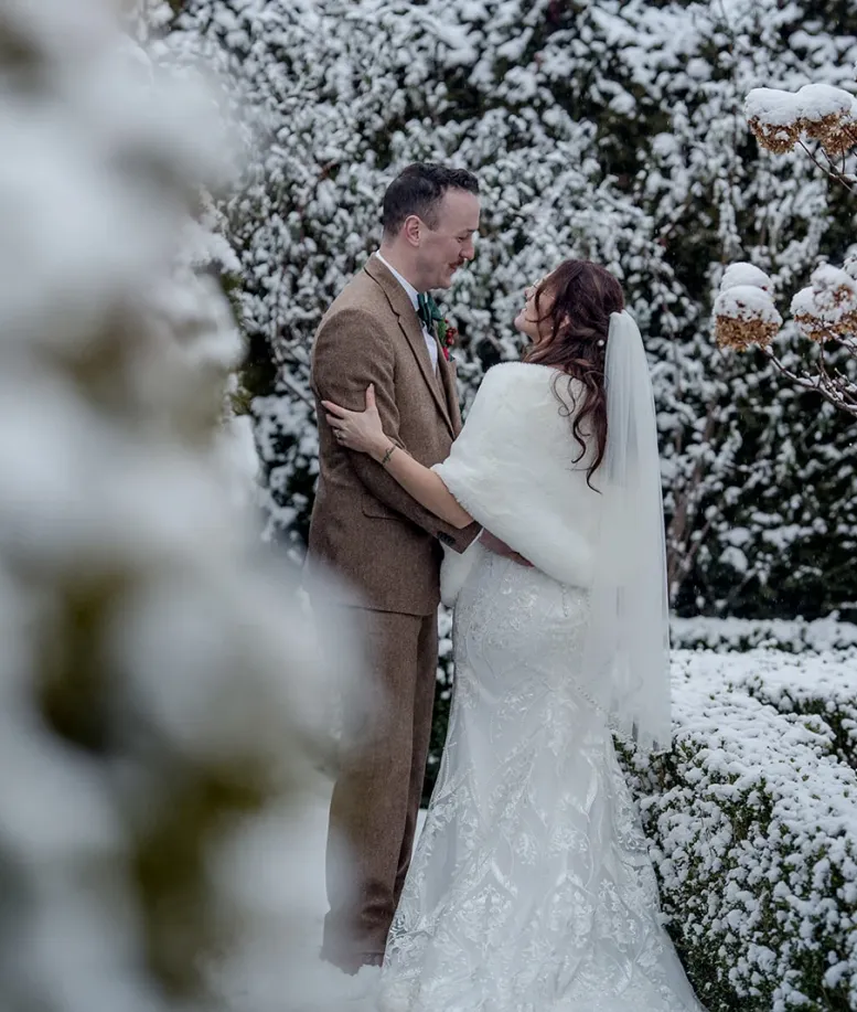 Bride and groom embracing in a snow-covered garden at Castle Farms. Photo credit: Paxton Photography.