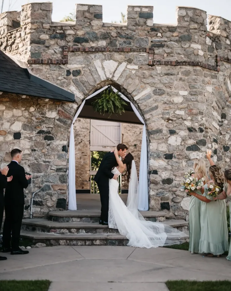 A bride and groom kiss at their wedding in front of a castle at Castle Farms.